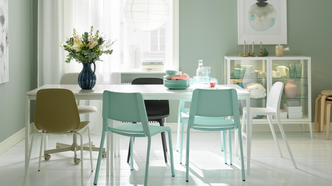Une zone salle à manger constituée de deux tables MELLTORP blanches alignées, une lampe REGOLIT blanche, des chaises assorties et des fleurs dans un vase.