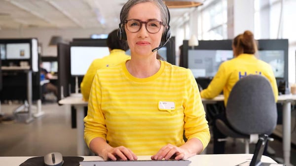 Un'esperta di acquisti da remoto di IKEA è seduta a una scrivania e indossa le cuffie.