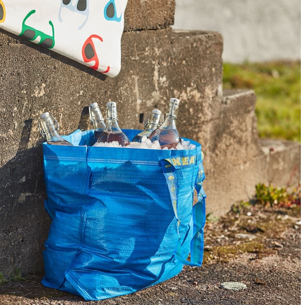 Unha bolsa de cor azul FRAKTA, chea de xeo e botellas de vidro, apoiada nuns chanzos de formigón.
