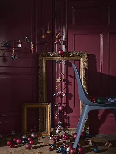 Unha cadeneta de decoracións e luces na árbore nun cuarto cunha cadeira e marcos de fotos dourados.