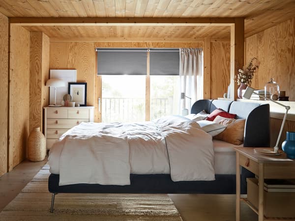Unha cama TUFJORD azul nunha habitación con paneis de madeira, cunha ventá detrás onde se reflicte a luz.