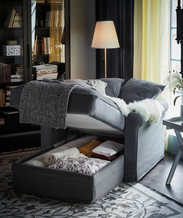 Unha chaiselongue GRÖNLID gris con almacenaxe integrada debaixo do asento, aberto para mostrar mantas e coxíns extra.