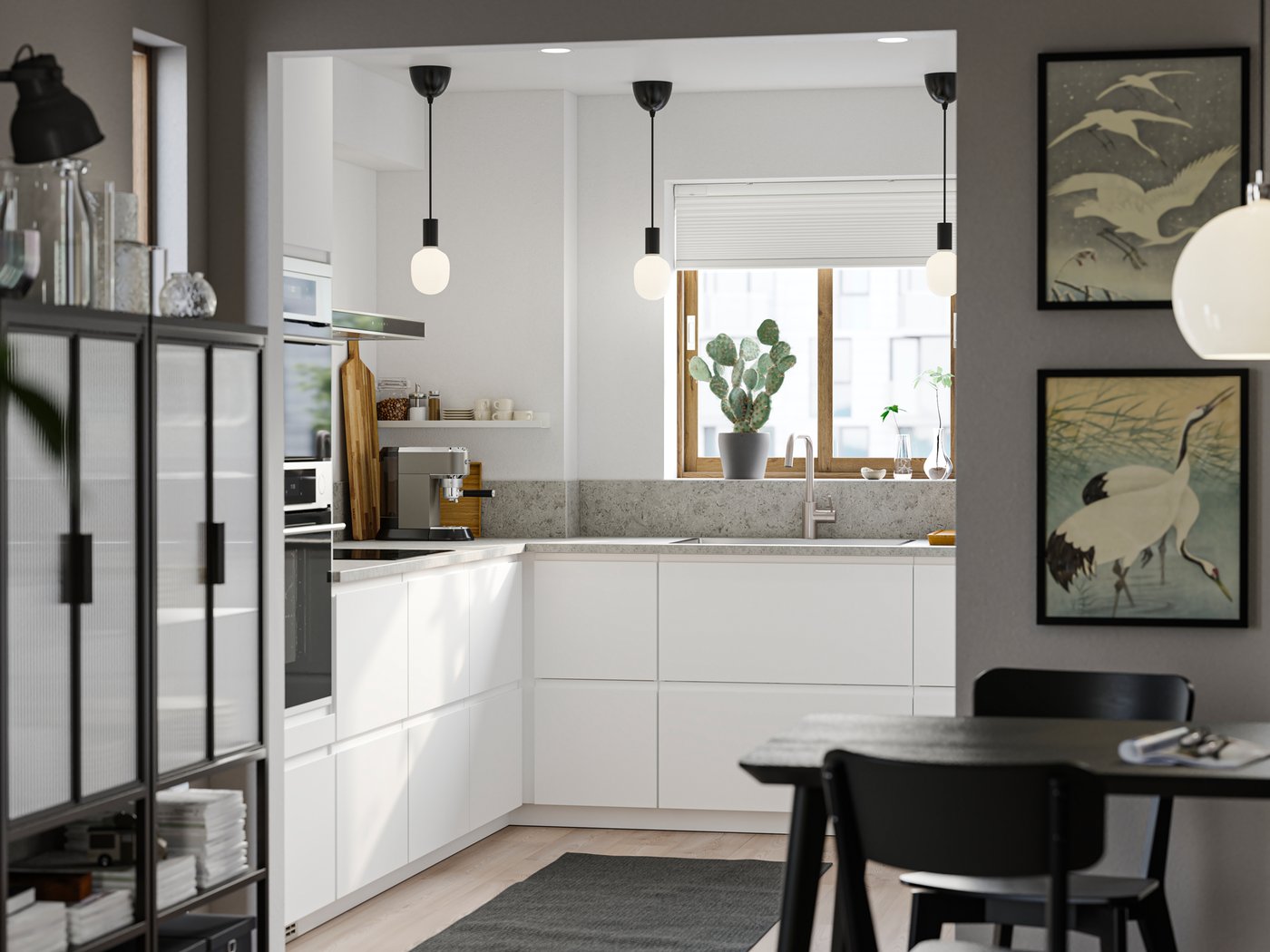 Unha cociña con frontes lisas VOXTORP en branco mate, con tres lámpadas colgantes negras en ringleira e unha zona de comedor en primeiro plano.