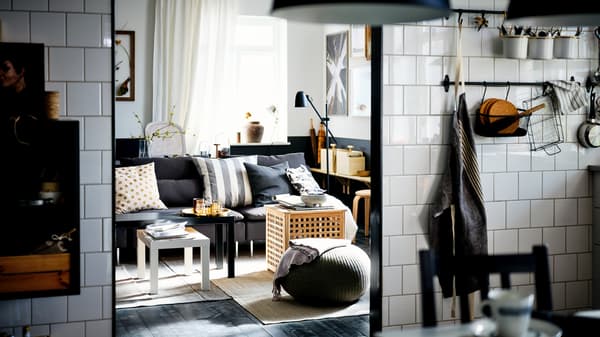 Unha cociña de azulexos brancos ábrese a unha sala de estar cun sofá SÖDERHAMN gris escuro e unhas mesas niño LACK en branco e negro.