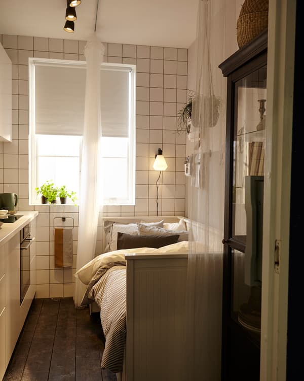 Unha cociña pequena utilizada como dormitorio temporal coa axuda dun sofá cama e unha cortina que as veces de separador de estancias.