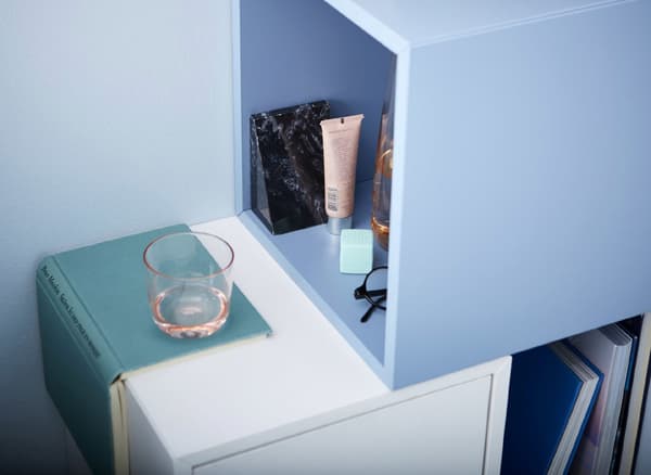 Unha combinación de mesa de noite feita con armarios de formas cúbicas con algúns tubos de cosméticos, uns lentes e un floreiro.
