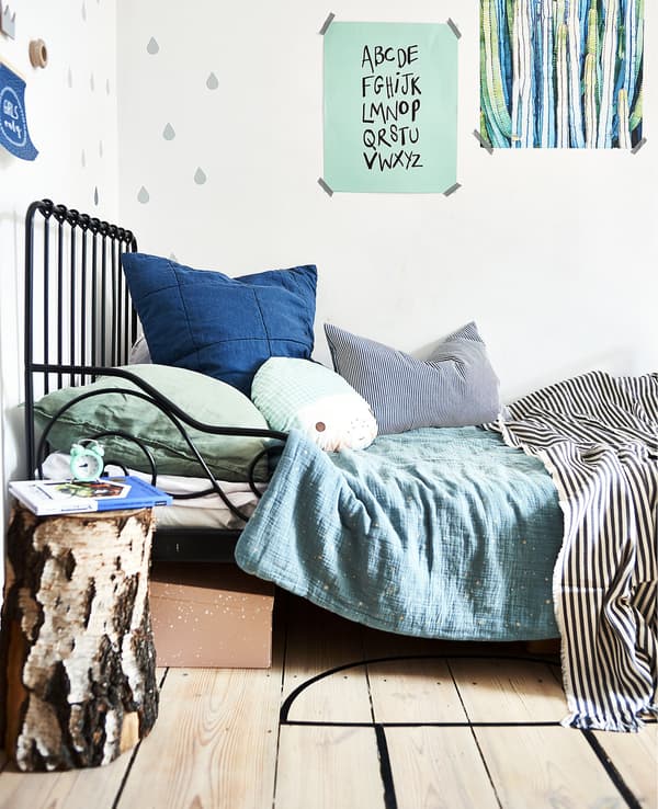 Unha estrutura de cama negra con roupa de cama verde e azul e láminas na parede.