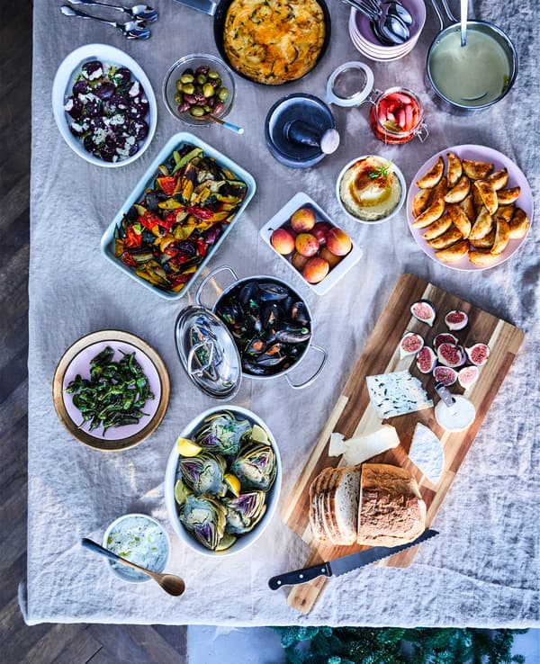 Unha mesa de bufete con comida variada servida en táboas de cortar e en pratos, vistos dende arriba.