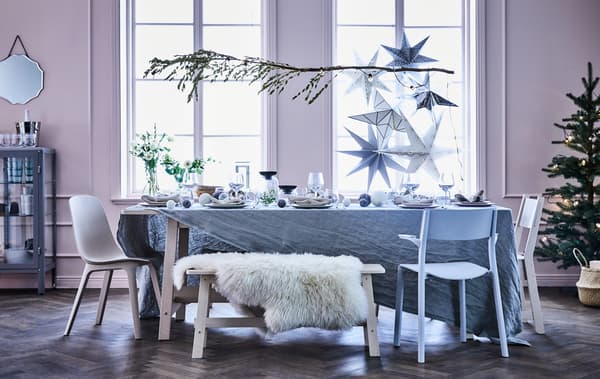 Unha mesa de comedor cun banco e cadeiras diferentes, sobre a mesa colga unha rama decorada cunha grilanda luminosa.
