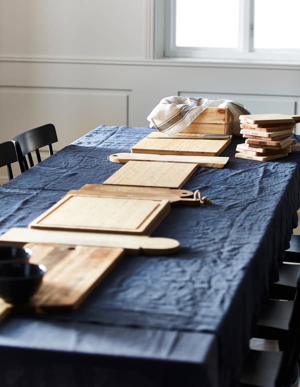Unha mesa de comedor cun mantel azul e táboas de cortar de madeira colocadas en liña no centro da mesa.