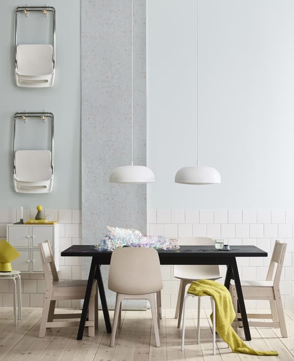Unha mesa de comedor negra de IKEA con seis cadeiras distintas brancas e marrón claro e dúas lámpadas de teito enriba.