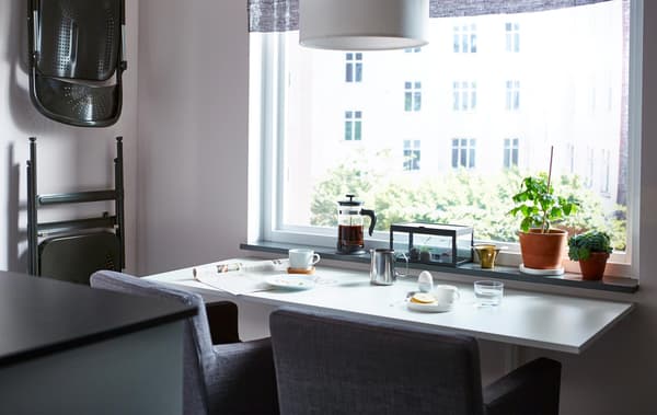 Unha mesa de comedor que ocupa pouco espazo, co almorzo preparado e dúas cadeiras fronte a unha fiestra.