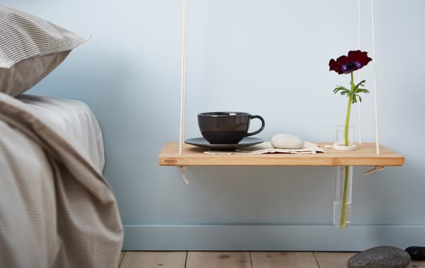 Unha mesa de noite colgante caseira feita cunha táboa de cortar e corda sobre unha parede azul claro nun dormitorio.