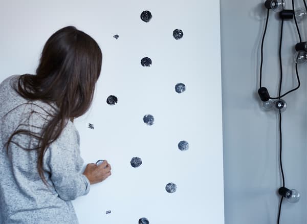 Unha muller facendo estampados de punto negro nunha folla de madeira contrachapada branca.