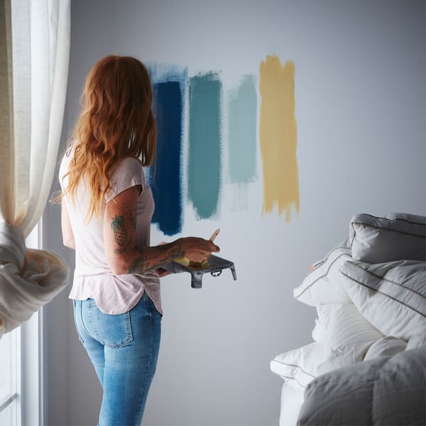 Unha muller proba varias cores de pintura para o seu dormitorio pintando tiras con elas na parede.