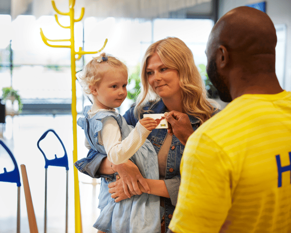 Unha muller suxeita a súa filla no colo. A nena está recollendo unha tarxeta agasallo de IKEA que lle está a dar un colaborador.