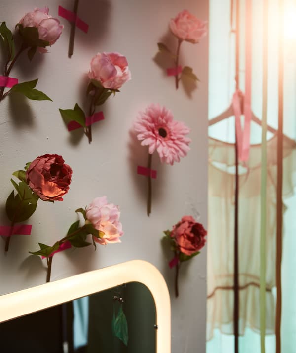 Unha parede cuberta de flores decorativas SMYCKA, pegadas unha a unha con adhesivo rosa.