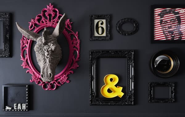 Unha parede negra decorada con distintos obxectos e marcos, con toques en cor rosa e amarelo.