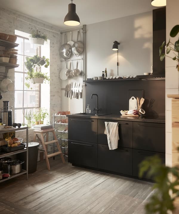 Unha pequena cociña negra IKEA METOD preto dunha ventá alta con utensilios colgados na parede.
