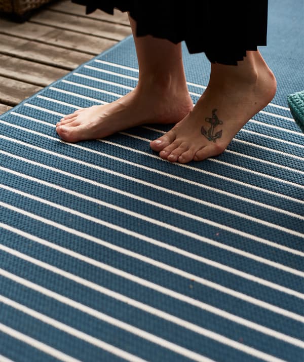 Unha persoa camiña descalza sobre unha alfombra de raias azuis e brancas.