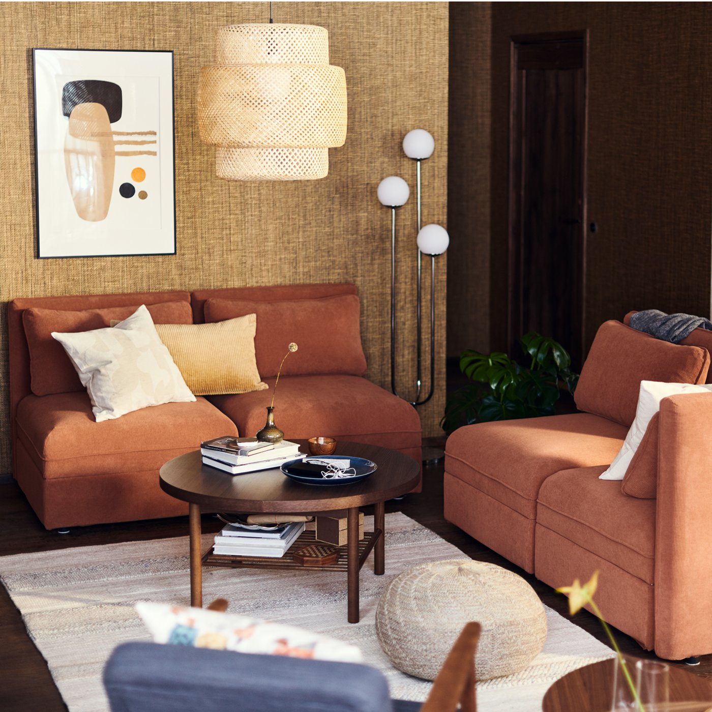 Unha sala de estar con sofás modulares VALLENTUNA vermellos debaixo dunha lámpada de teito SINNERLIG de bambú.