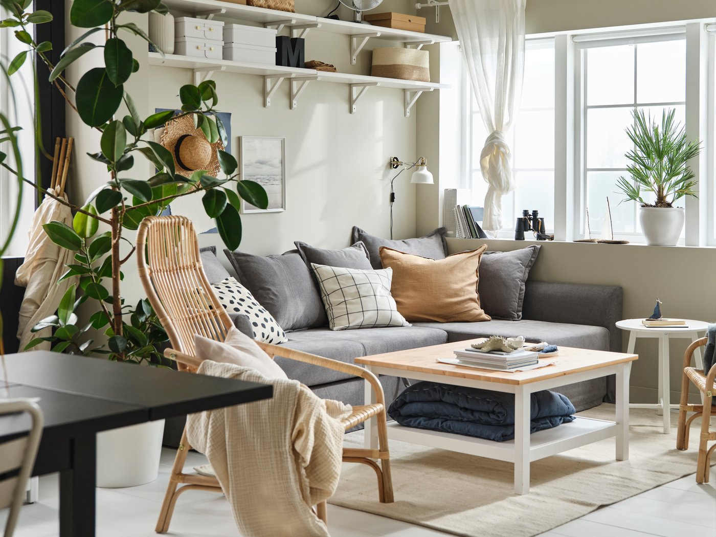 Unha sala de estar luminosa con grandes fiestras, un sofá cama de esquina HOLMSUND e unha mesa de centro HEMNES, artigos téxtiles e plantas grandes.