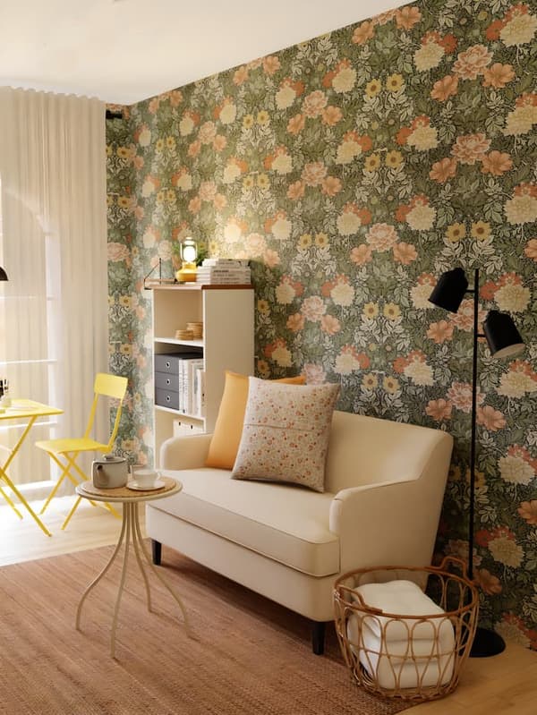 Unha sala de estar tradicional con paredes cun papel pintado de flores con tons verdes e pastel. Un sofá beixe ROCKSJÖN con coxíns, sobre unha alfombra de fibras STRÖG.