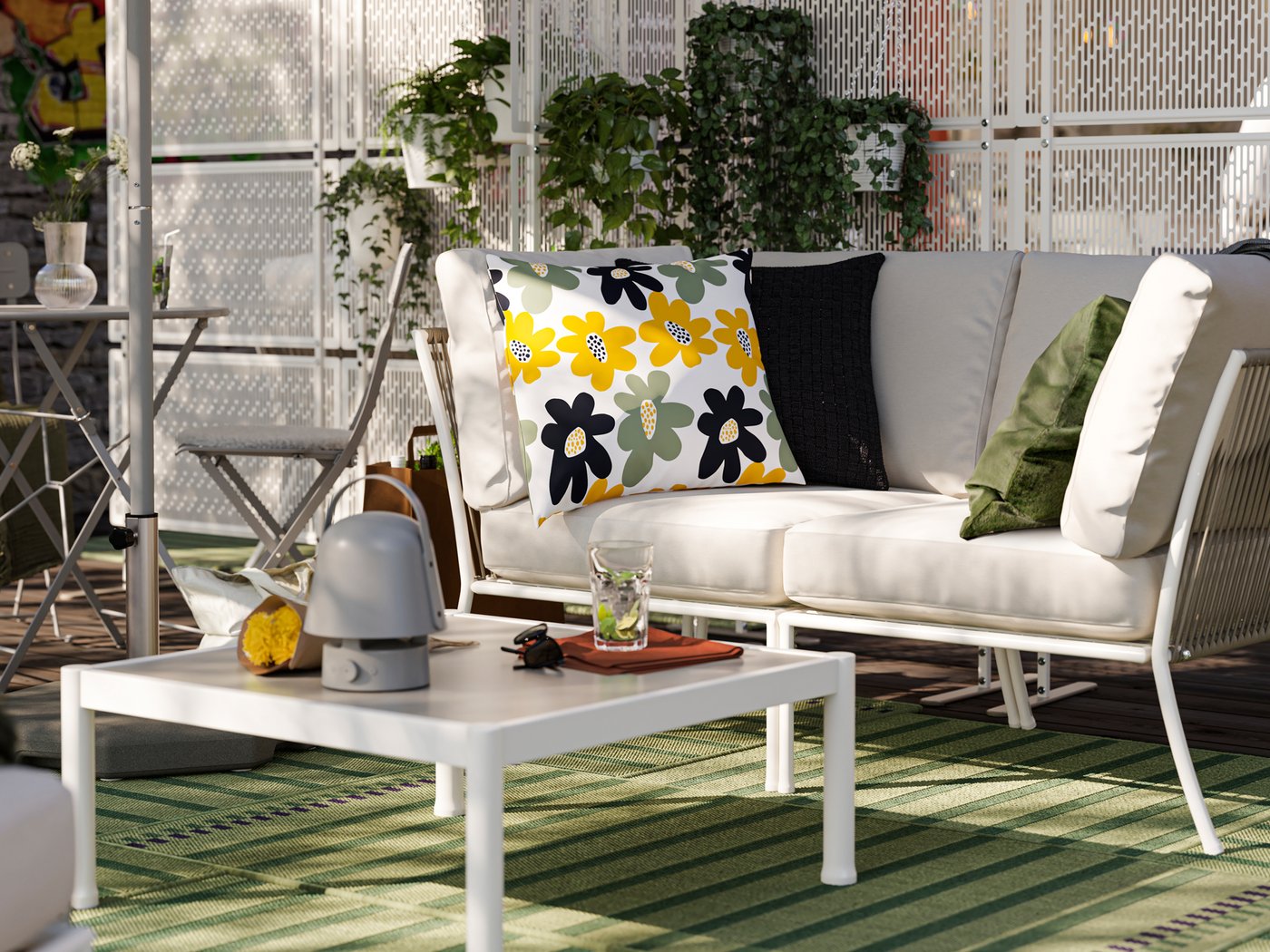 Unha terraza cun sofá SEGERÖN e unha mesa de centro. Hai alfombras de exterior verdes e pantallas de privacidade con plantas.
