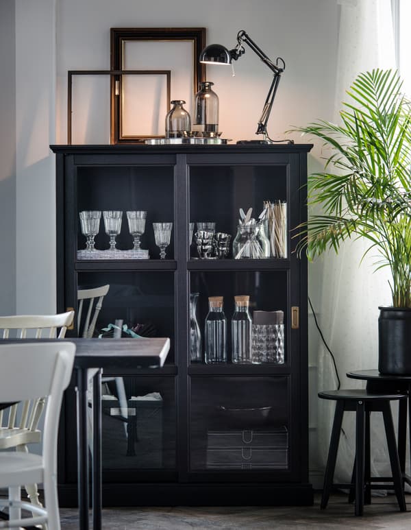 Unha vitrina contén vasos, pratos e obxectos decorativos nun comedor branco.