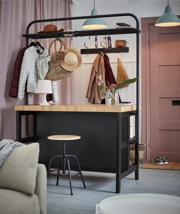 Un'isola cucina con rastrelliera VADHOLMA che separa due ambienti. Sono appesi cappelli, borse e vari indumenti.