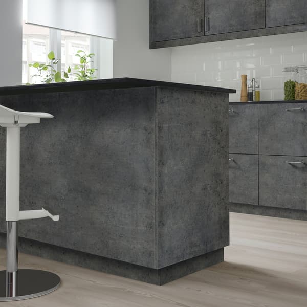 Un'isola in una cucina KALHYTTAN grigio scuro effetto cemento con davanti uno sgabello bianco.