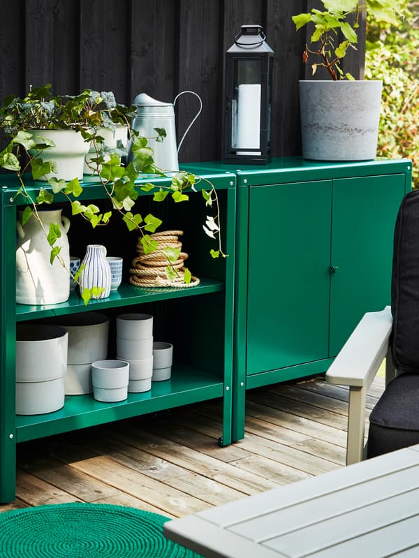 Unités de rangement vertes à l’extérieur, avec divers pots, pichets et cache-pots, une lampe et quelques sets de table.