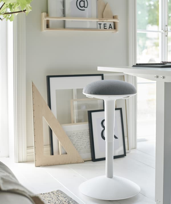 Uno sgabello bianco e grigio vicino a una scrivania bianca e dei quadri appoggiati alla parete - IKEA