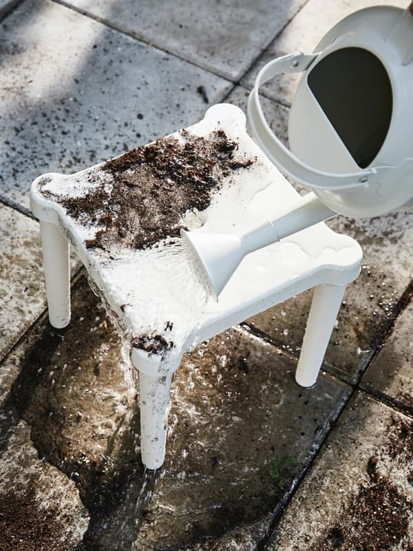 Uno sgabello bianco sporco di terra che viene pulito con dell'acqua versata da un'annaffiatoio.