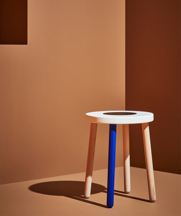 Uno sgabello di legno con una gamba blu e la seduta bianca in una stanza arancione.