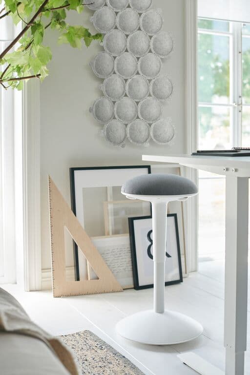 Uno sgabello NILSERIK di fronte ad un bancone. Sulla parete di fondo è appeso un pannello fonoassorbente. Sul pavimento sono appogiate cornici con stampe e una riga in legno.