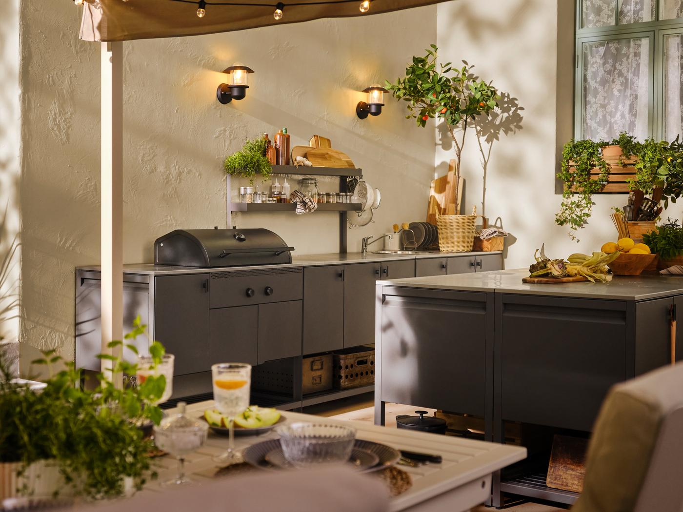 Uno spazio esterno con una cucina BÅTSKÄR: barbecue a carbonella, elemento per il lavello, mobile con ante per la cucina ed elemento supplementare con ripiani - IKEA.