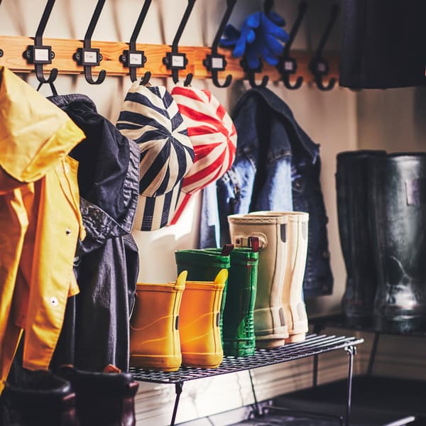 Unos cuantos pares de botas colocados en dos zapateros GREJIG que están sobre un tapete para limpiarse los zapatos debajo de dos percheros KARTOTEK montados en la pared.