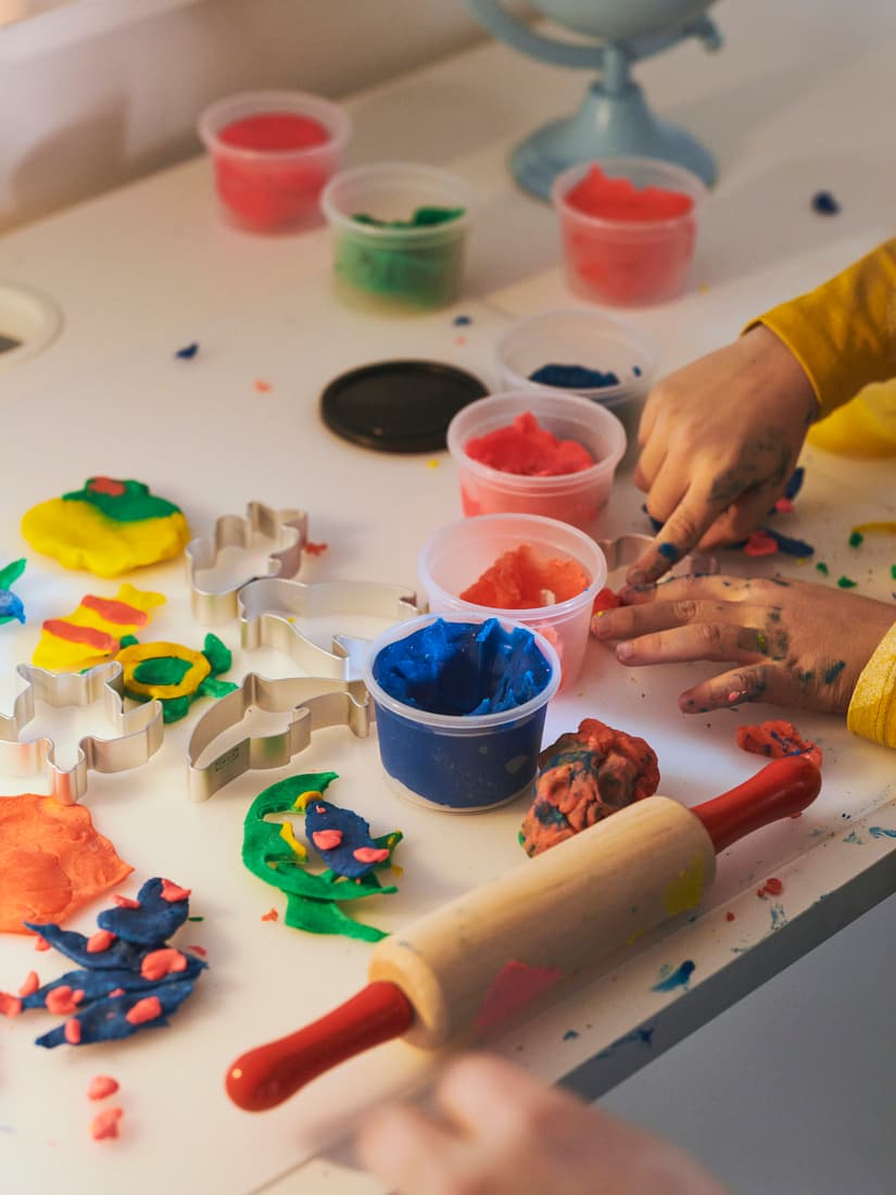 Unos niños jugando con masitas de colores sobre una mesa.
