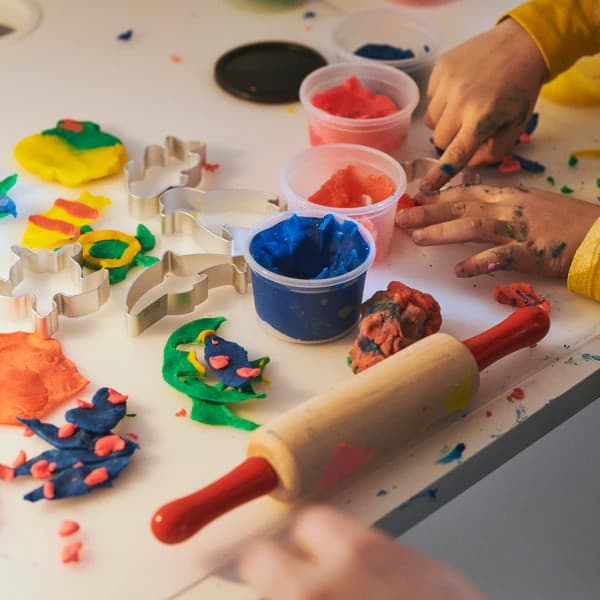 Unos niños jugando con unas masas de colores en una mesa.