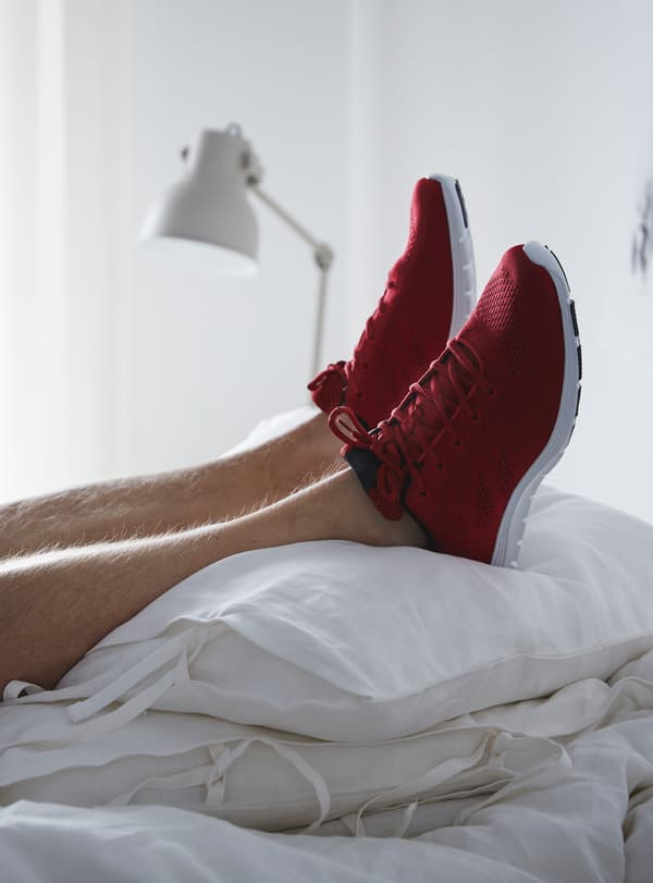 Unos pies con zapatillas deportivas de color rojo brillante descansan sobre una pila de almohadas blancas.