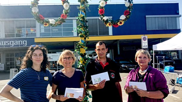 Unter dem IKEA Midsommarbaum stehen 4 Menschen bei der Geldübergabe. Die Menschen die die drei Vereine vertreten haben Umschläge mit Geld in den Händen, die andere Person ist die Vertreterin von IKEA. 