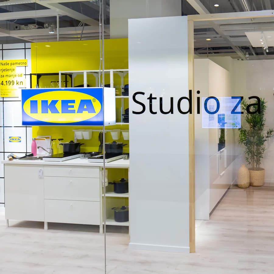 Unutarnji prostor IKEA trgovine s bijelim kuhinjskim namještajem, žutim zidovima i natpisom “Studio za planiranje”. Scena prikazuje izložbeni prostor s modernim dizajnom.