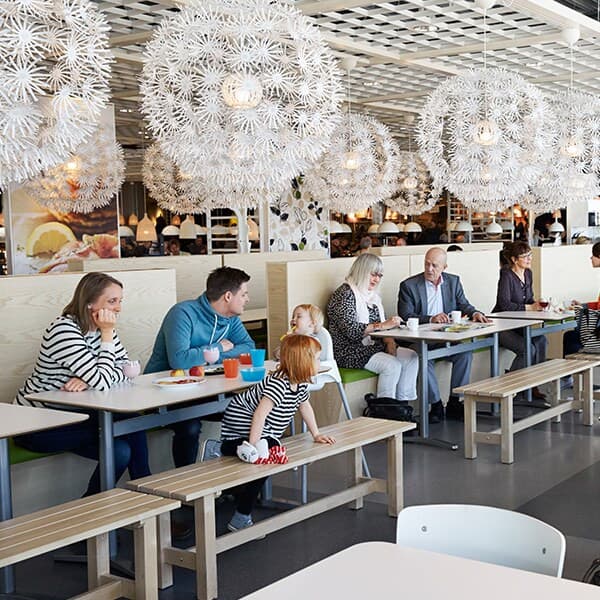 Unutrašnjost restorana s ljudima koji sjede za drvenim stolovima. Velike bijele svjetiljke vise sa stropa, a dijete hoda između stolova.