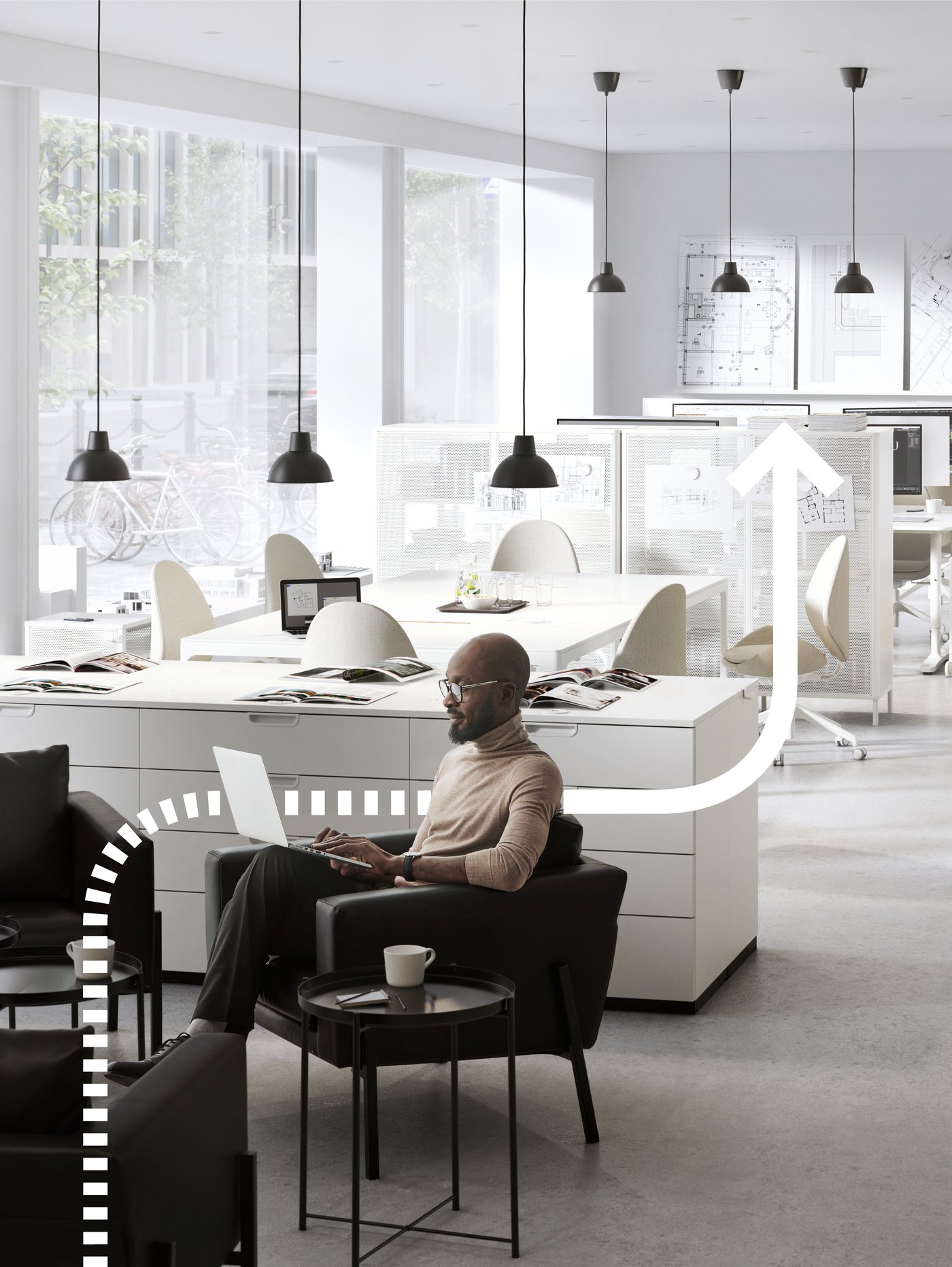 Uomo seduto su una poltrona nera in un ufficio luminoso con arredamento bianco e laptop sulle ginocchia.
