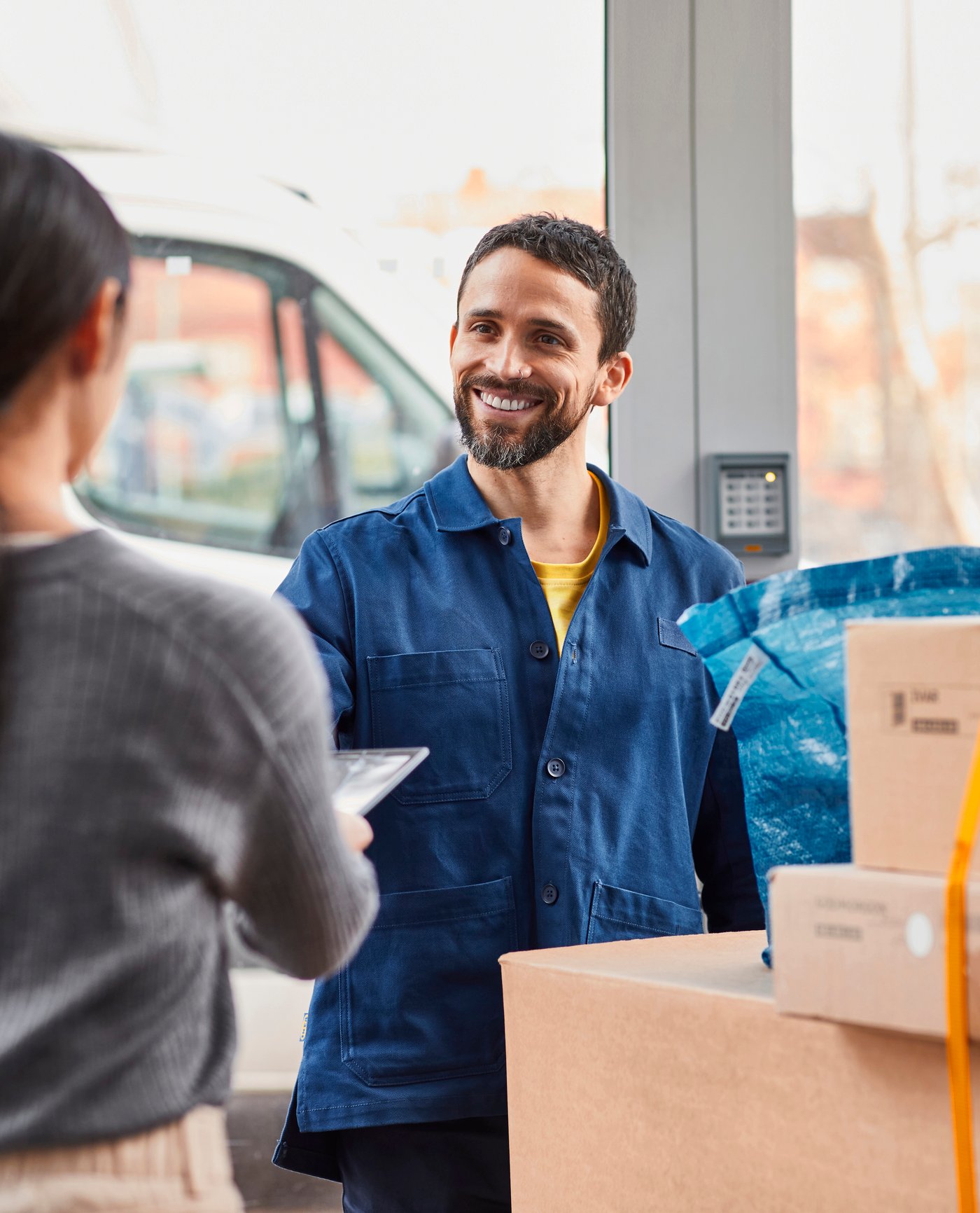 Uomo sorridente con divisa blu che consegna scatoloni e borse.