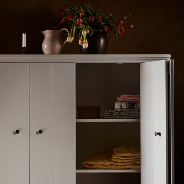 Upper corner of a grey IDANÄS cabinet, one folding door open to reveal table textiles inside. Vases with flowers on top.