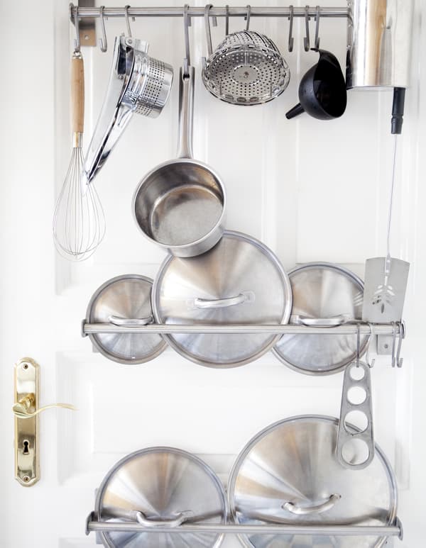 Ustensiles et couvercles de casseroles rangés sur des barres fixées à une porte.