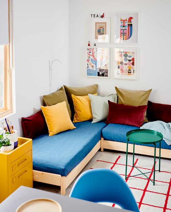 UTÅKER stackable bed is used as a corner sofa and has blue bedspreads and many cushions. A green tray table stands beside.