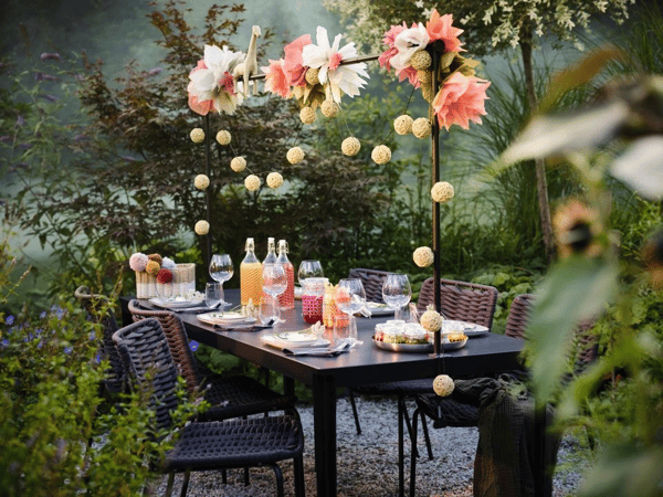 Utomhusdukning med svart bord och fyra stolar. Bordet är dekorerat med blommor, hängande bordsdekorationer och flaskor samt glas för dryck.